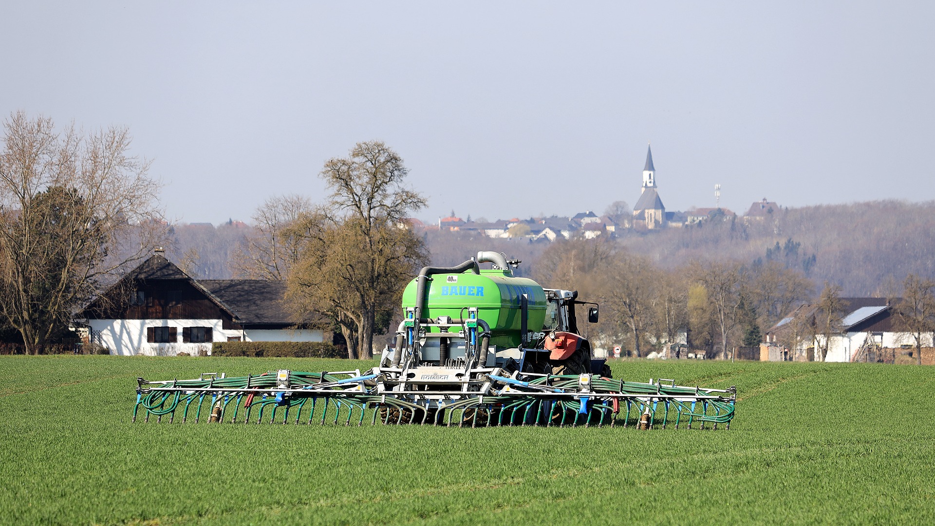 Ein Traktor fährt mit Güllefass über ein grünes Feld. Die Gülle wird durch modernste Technik bodennah und emissionsarm ausgebracht.