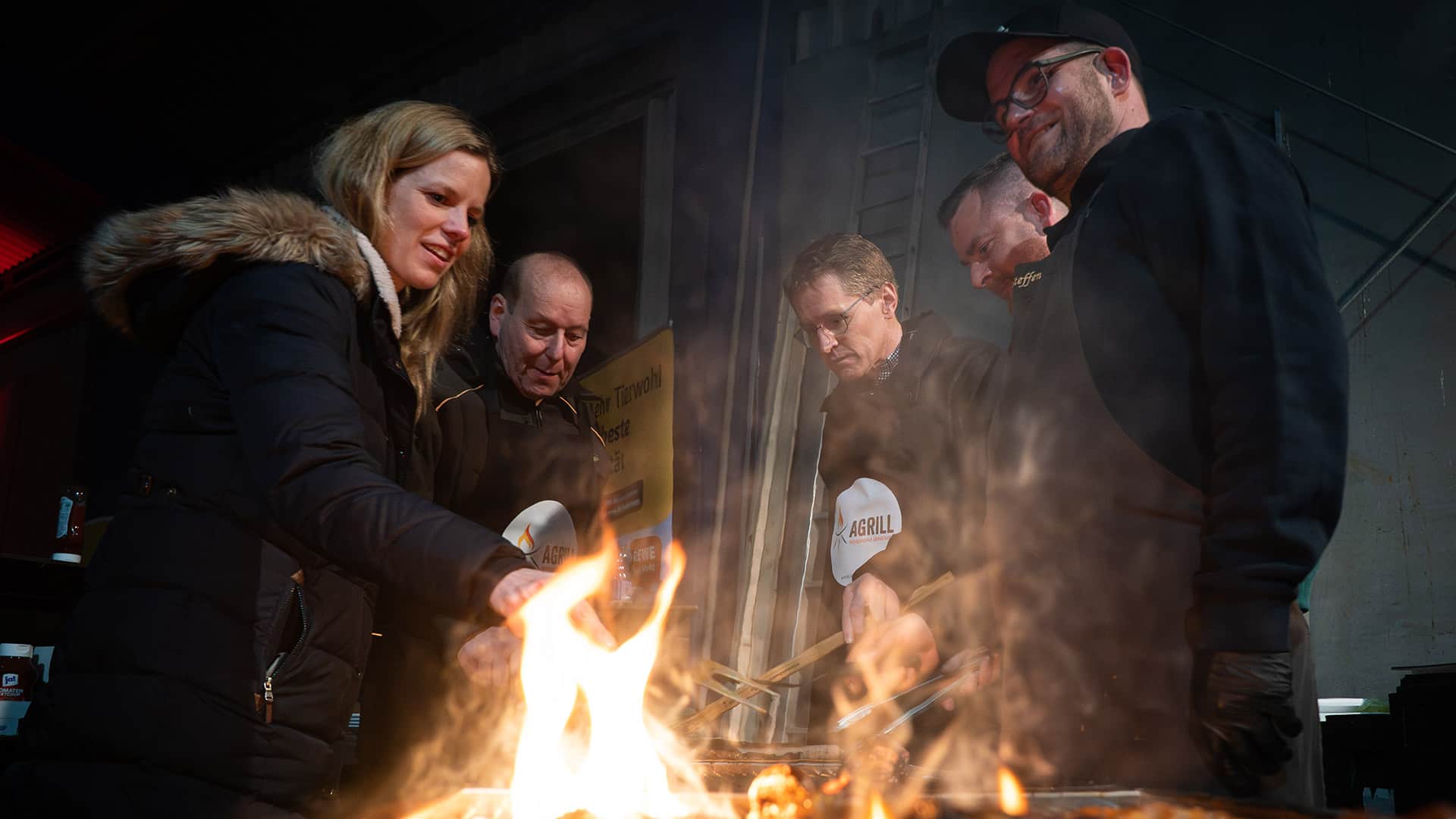 Personen grillen im Rahmen des AGRILL gemeinsam an einem Grill auf einem landwirtschaftlichen Hof